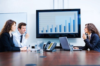 Three people gathered around a larrge screen monitor to discuss business improvement, representing a Customer Success Manager at work.