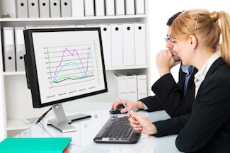 Two business people looking at a spreadsheet on a monitor, representing a customer success manager working directly with a client.