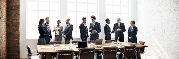 A group of business people standing around a boardroom table; representing The Mission of Customer Success