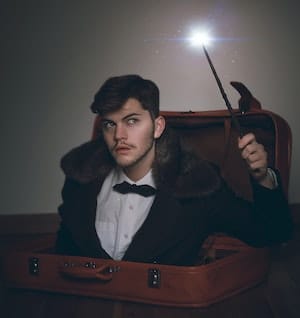 Magician holding wand coming up from open suitcase