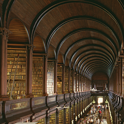 Image of Trinity Library in Dublin showing bookcases filled with very old books under a wood paneled vaulted roof